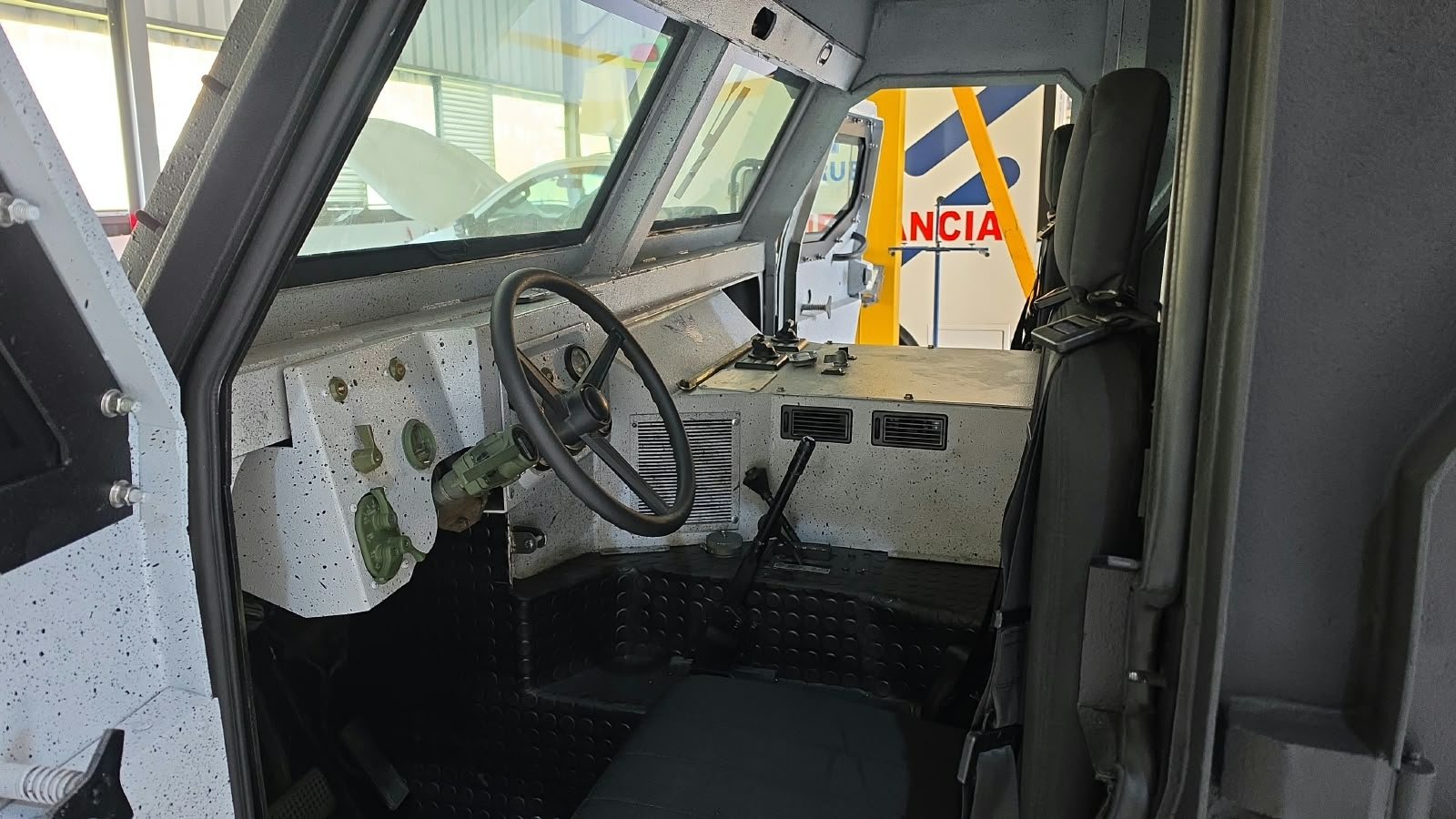 Puesto de conducción de un vehículo blindado visto desde el asiento trasero, con volante y tablero
